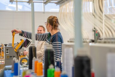 Bedrijkskledingshop Assen: Toont werkvloer met borduurmachines, tafels en een trap, in een goed verlichte omgeving